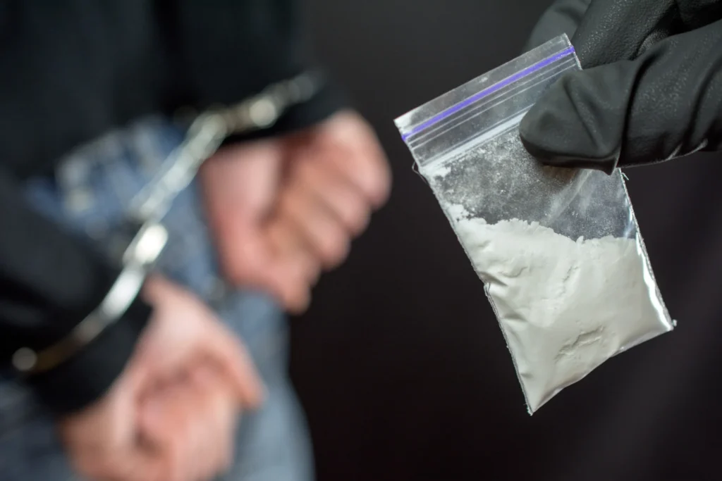 Close-up of a handcuffed person with a gloved officer holding a small plastic bag of white powder, symbolizing a drug-related arrest in Tacoma.