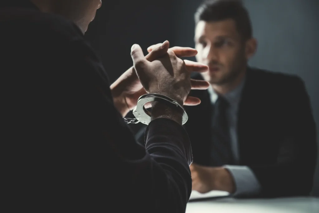 A man in handcuffs sitting and talking to his criminal defense lawyer.