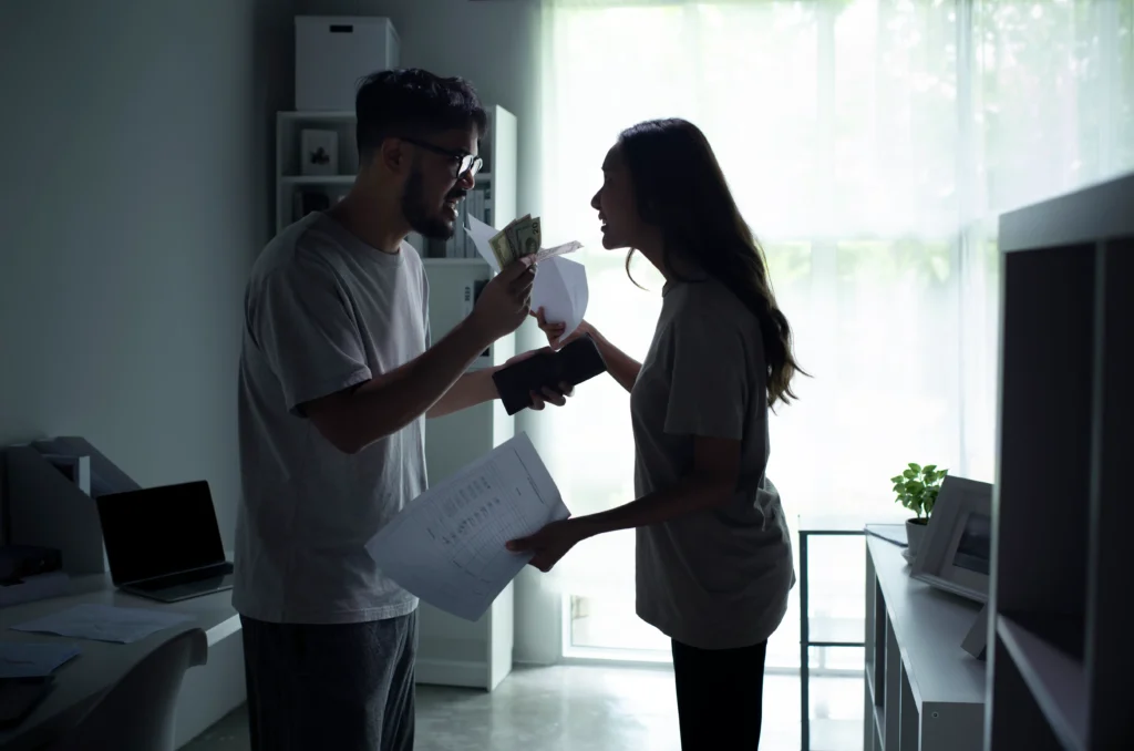 Couple arguing intensely indoors while holding cash and documents, illustrating financial conflict or domestic dispute.